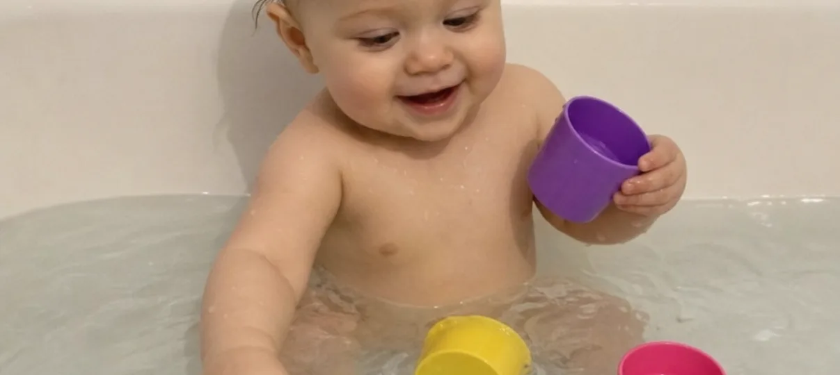 Baby playing with floating bath cups in a bathtub