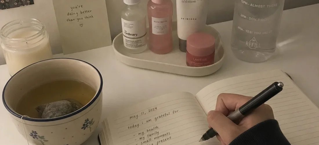 Calm Self-Care Wellness Setup Person journaling beside tea, skincare items, and a water bottle